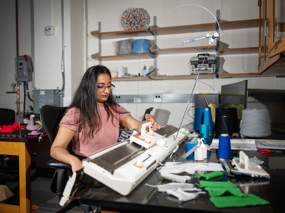 Krishma Singal sitting at a knitting machine