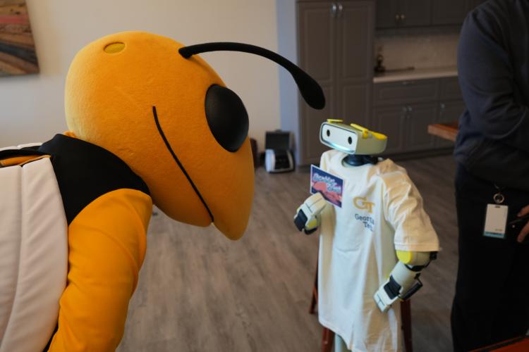 Photo of Buzz the mascot leaning down toward a small humanoid robot wearing a Georgia Tech t-shirt