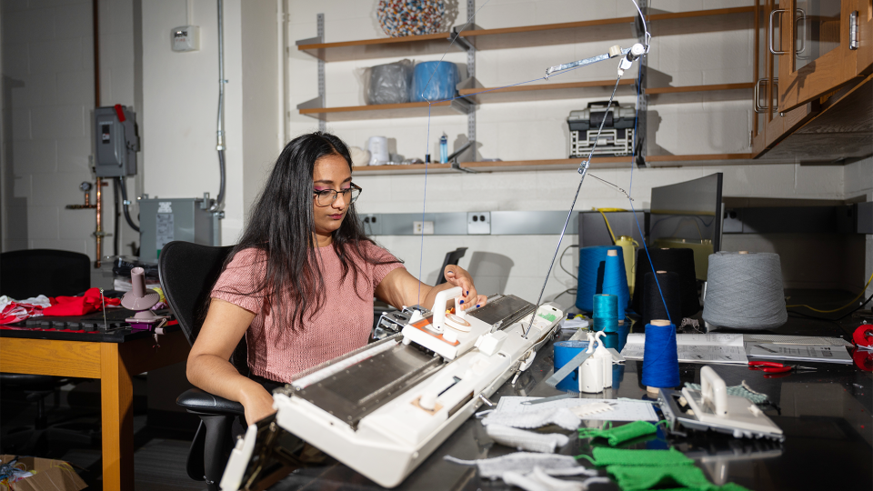 Krishma Singal sitting at a knitting machine