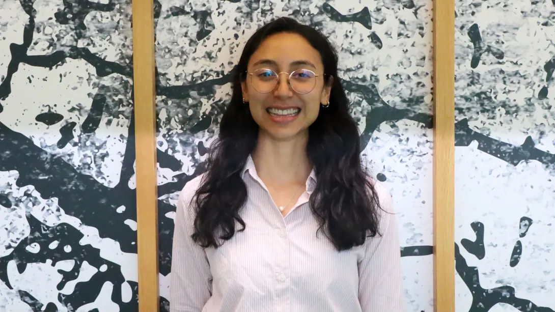 A smiling woman standing in front of a wall. The wall has a unique pattern and wood frames.